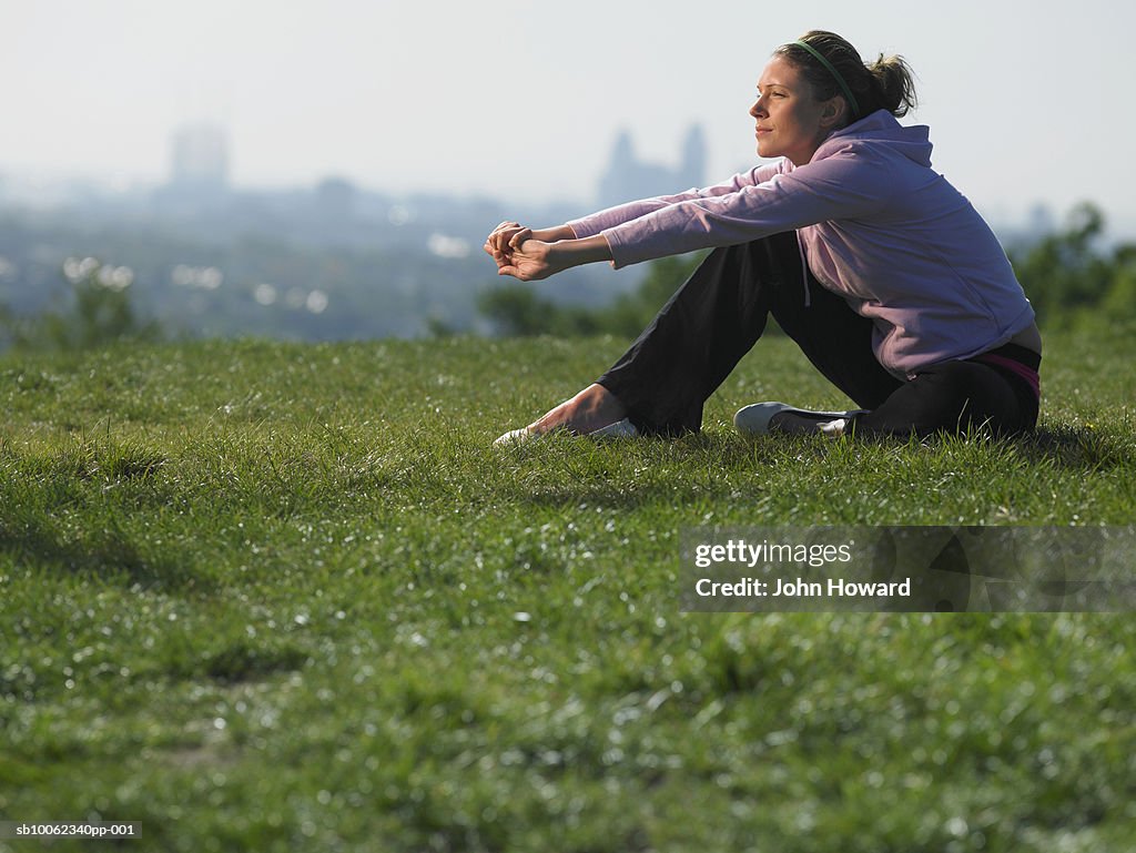 Young woman sitting on grass in sport clothes, cityscape in background