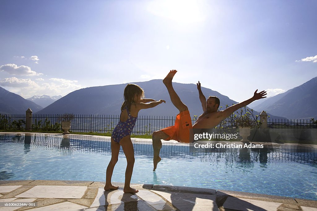 Daughter (4-5) pushing father into swimming pool