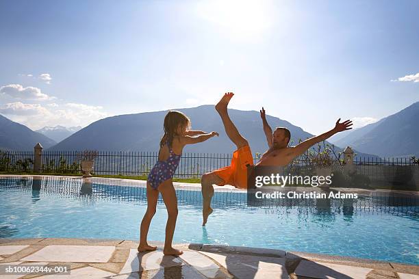 daughter (4-5) pushing father into swimming pool - shorts down stock pictures, royalty-free photos & images