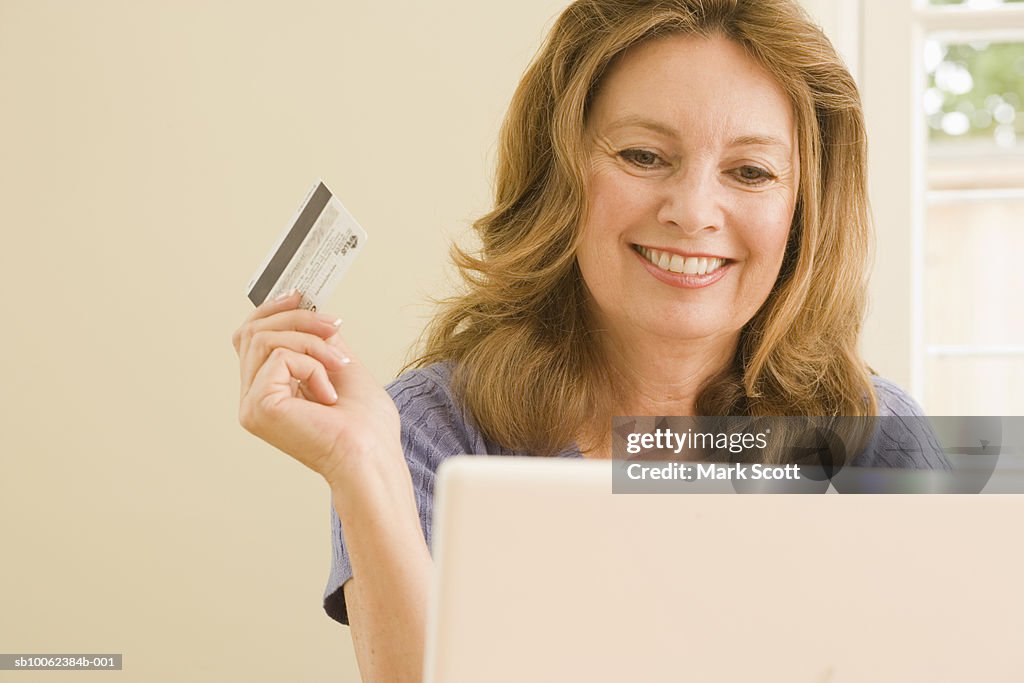 Mature woman sitting on front of laptop, holding credit card and smiling