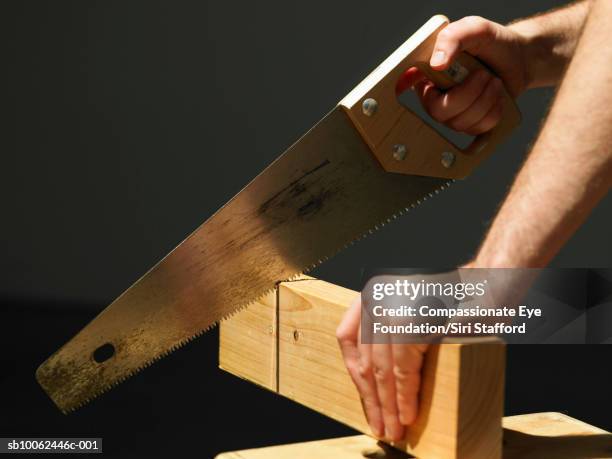 man cutting through block of wood using saw, close-up of hands - hand saw stock pictures, royalty-free photos & images