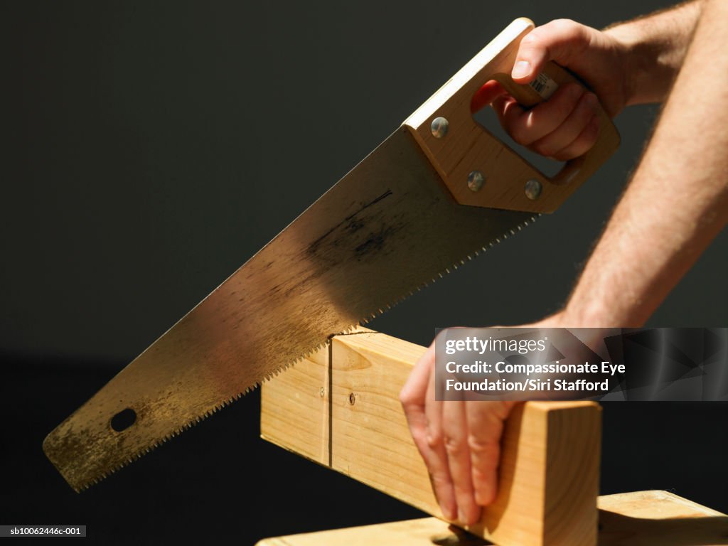 Man cutting through block of wood using saw, close-up of hands