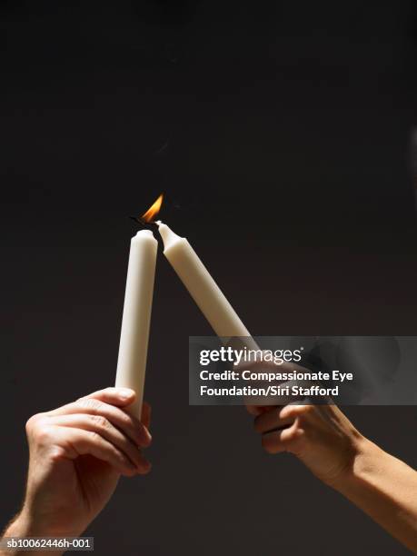 person holding aloft burning candle, trying to light another one, close-up of hands - lighting candle stock pictures, royalty-free photos & images