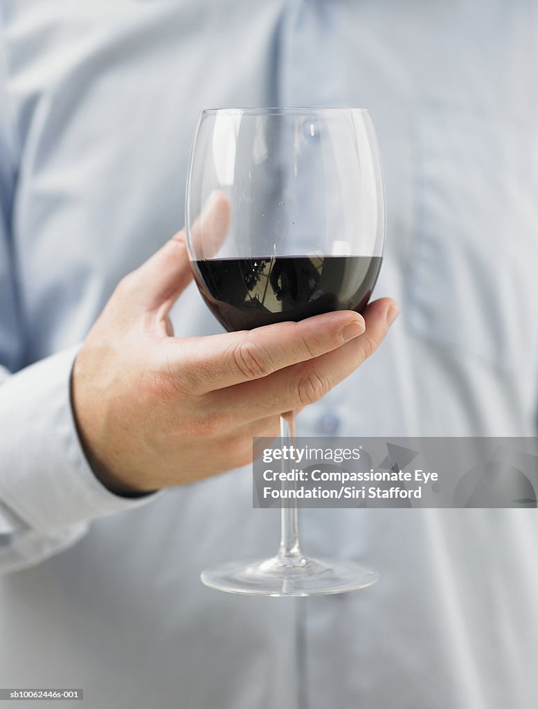 Man holding glass of red wine, mid section