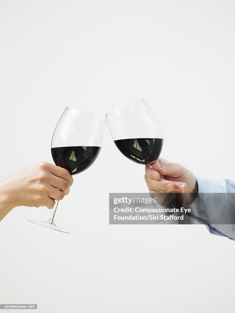 Man and woman toasting with red wine, close-up of hands, side view