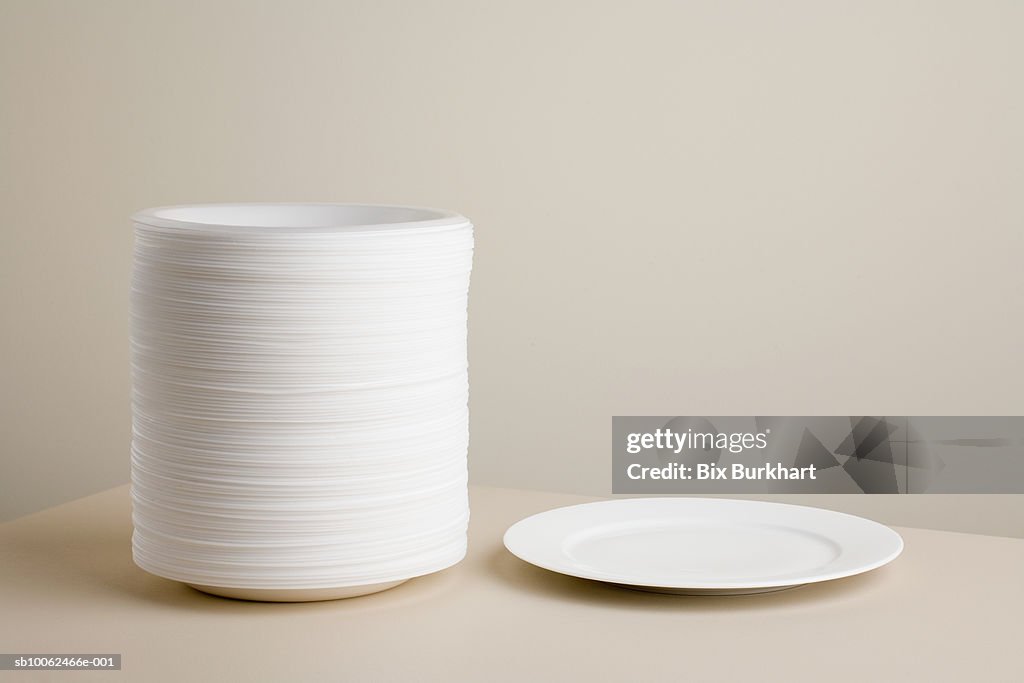 Stack Of Styrofoam Plates Beside Ceramic Plate On Table High-Res