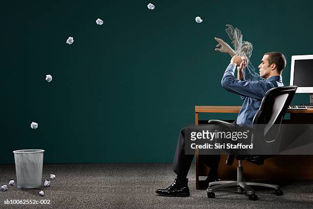 businessman sitting in office, throwing paper ball in dustbin - throwing fotografías e imágenes de stock
