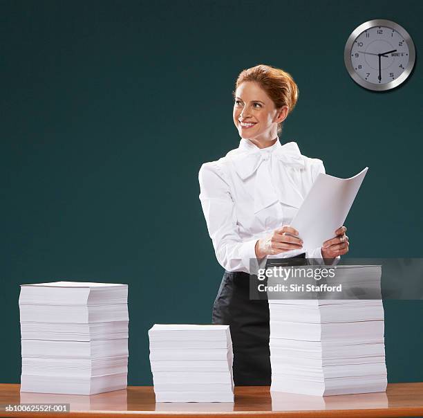 businesswoman holding sheets of paper, looking away, smiling - papierstapel stock-fotos und bilder