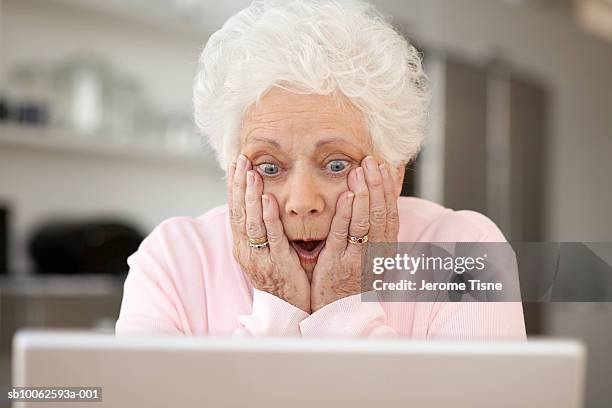 senior woman looking at laptop with head in hands and open mouth - terrified stock pictures, royalty-free photos & images