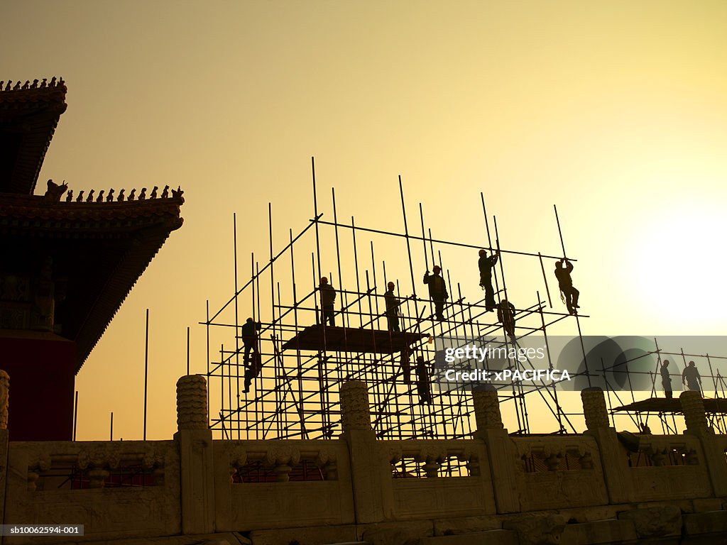 Silhouette of workers building scaffolding, low angle view