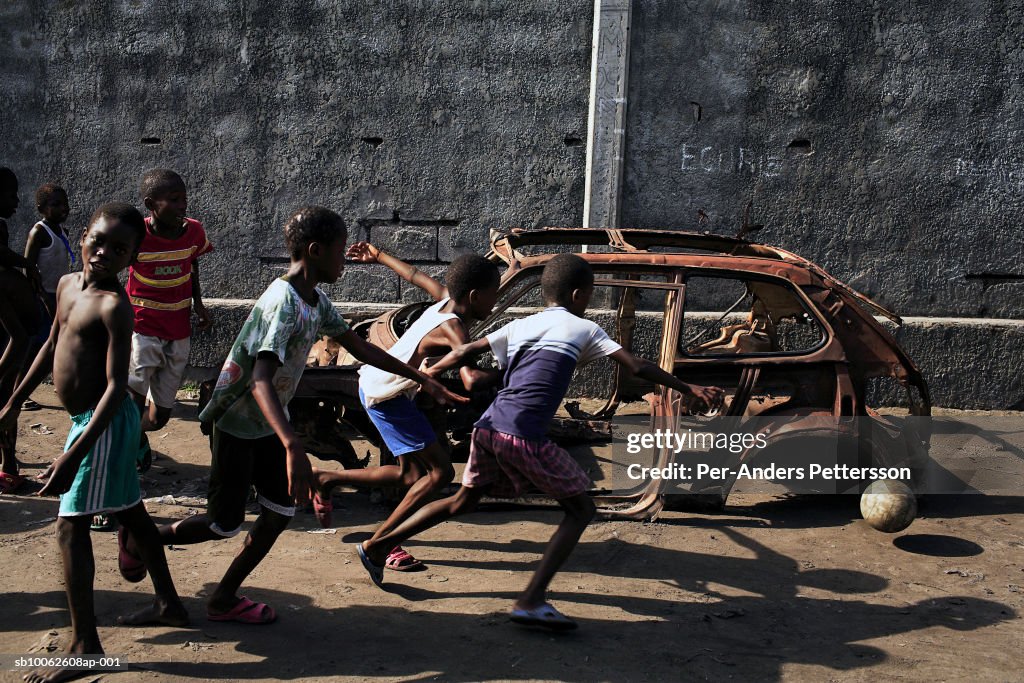 Boy (6-9) playing soccer by wreck of car