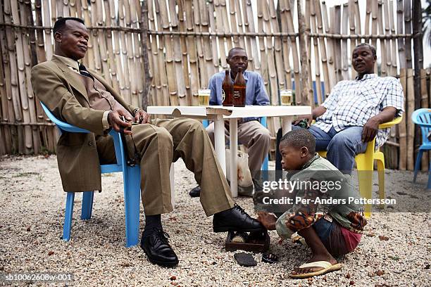 Shoeshine boy cleans a pair of shoes for a businessman in a bar on March 4, 2006 in Kisangani, in Congo, DRC. Kisangani is a port city along the The...