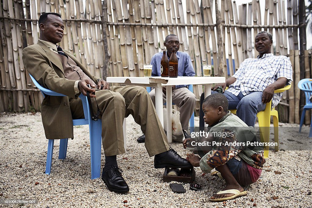 Shoeshine boy cleans shoes for businessman in bar