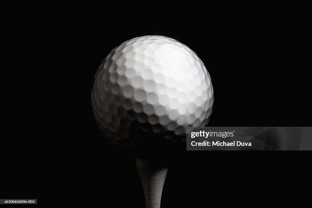 Golf ball on tee against black background, close-up