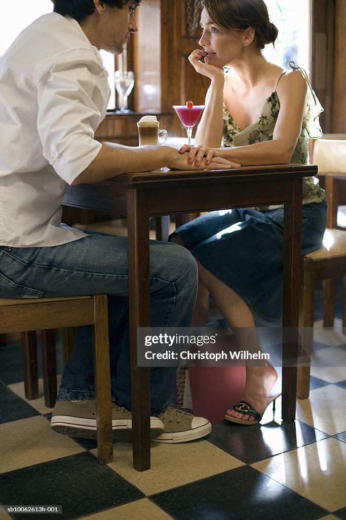 Couple sitting at table in cafe, holding hands, side view