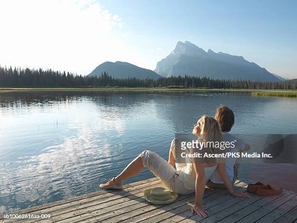 mature couple sitting on jetty by mountain lake - couple jetty stock pictures, royalty-free photos & images