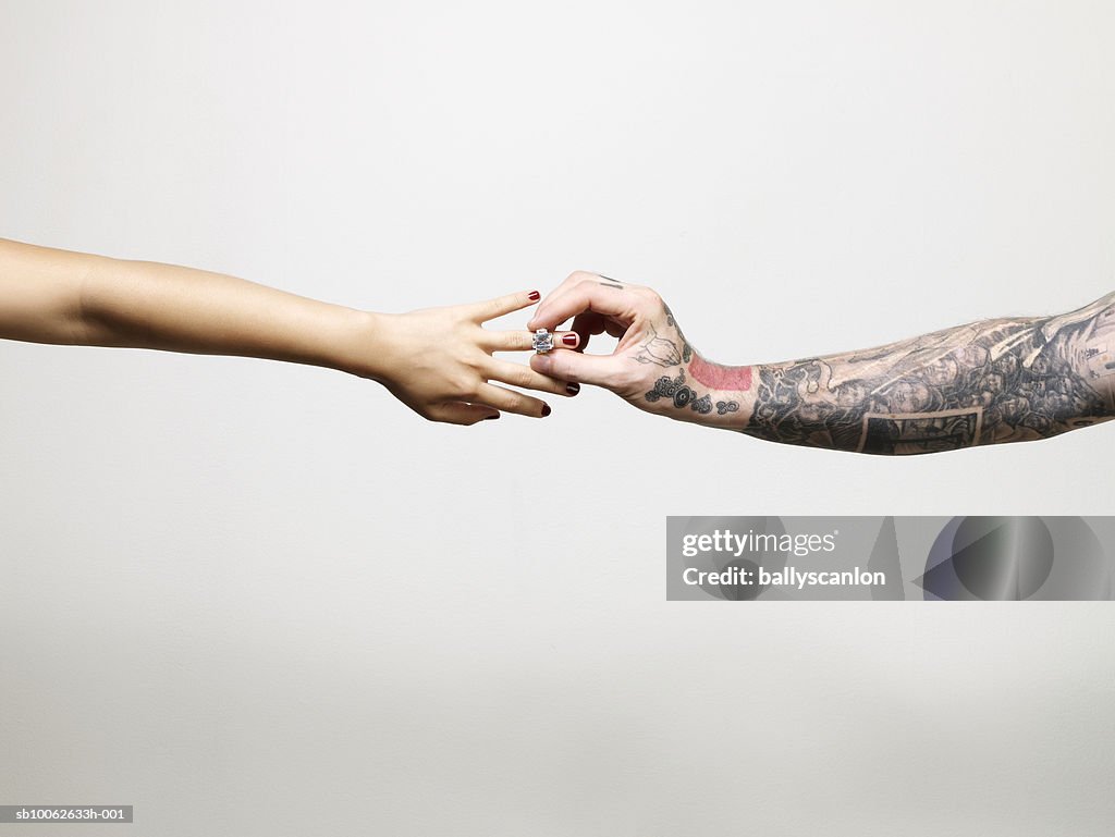 Man with tattooed arm placing ring on finger of young woman, close-up of arms and hands