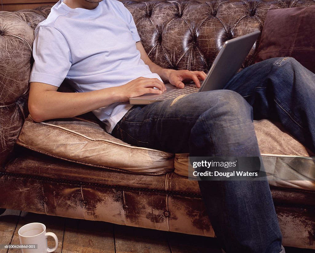 Young man sitting on sofa, using laptop, low section