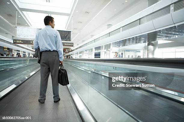 business man at airport, carrying briefcase, rear view - travolator stock-fotos und bilder