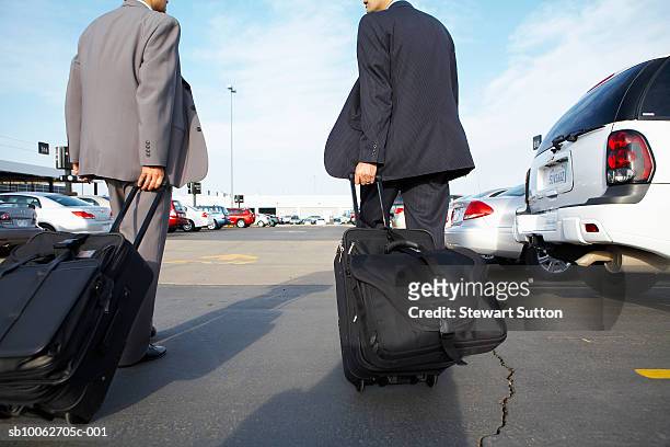 two business men pulling suitcases through car rental lot, rear view - auto mieten stock-fotos und bilder