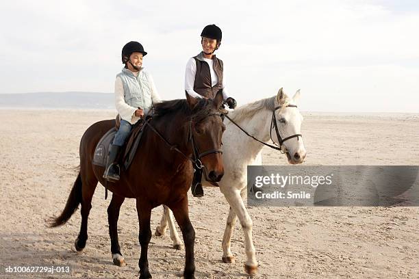 mother and daughter (6-7) riding horses on beach - horseback riding stock pictures, royalty-free photos & images