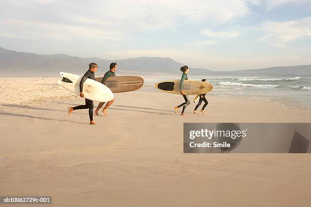 parents with son (14-15) and daughter (6-7) running into sea with surfboards - family smile photos et images de collection