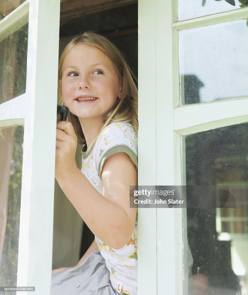 Girl (6-7) opening and looking out window, outdoors