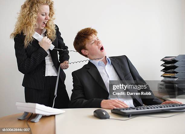 businesswoman pulling a telephone cord around businessman's neck at desk - women being strangled foto e immagini stock