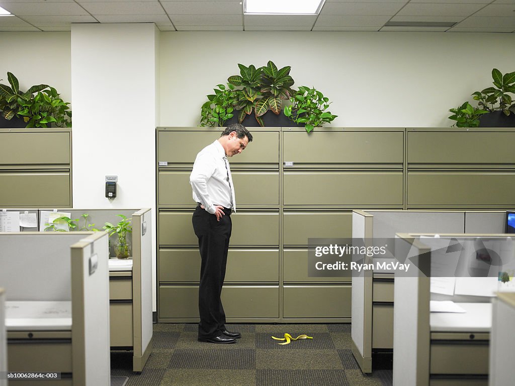 Businessman stares at banana peel in corridor