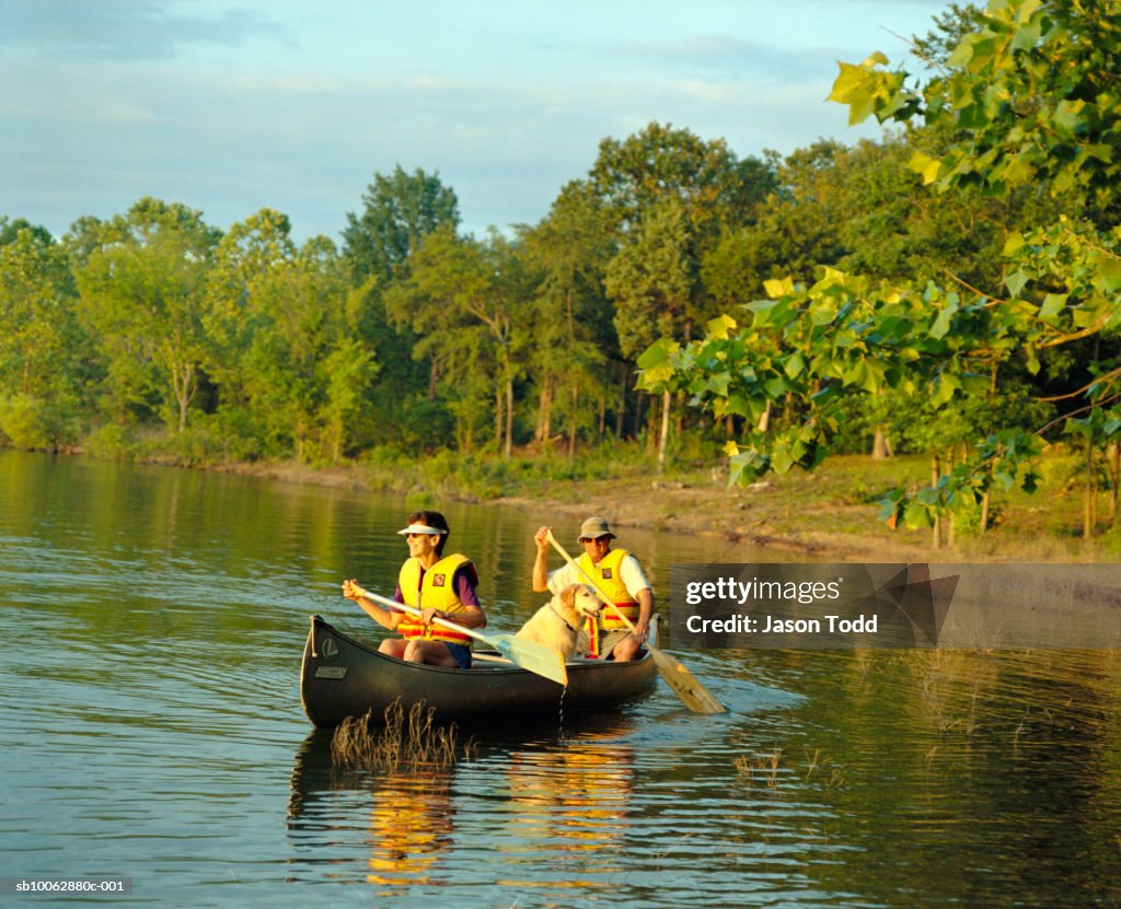 Mature couple with dog in canoe on lake, sunset