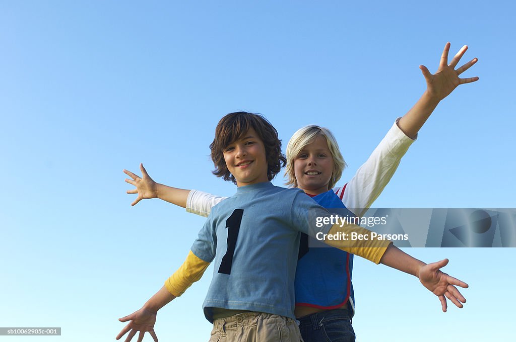 Two boys (11-13) raising arms against clear sky, portrait, low angle view