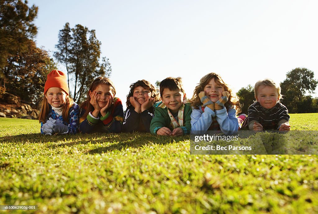 Group of children (5-7) lying on grass in park, portrait (surface level)