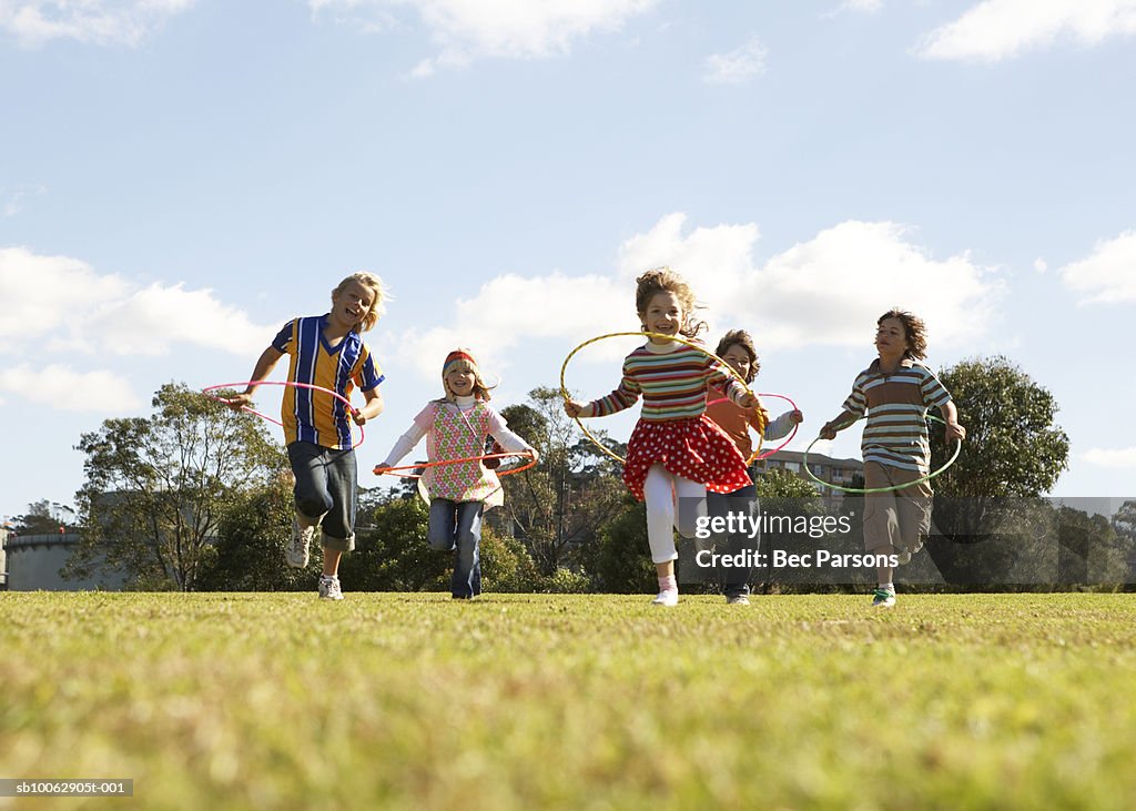 Five children (7-11) running with plastic hoops in park (surface level)