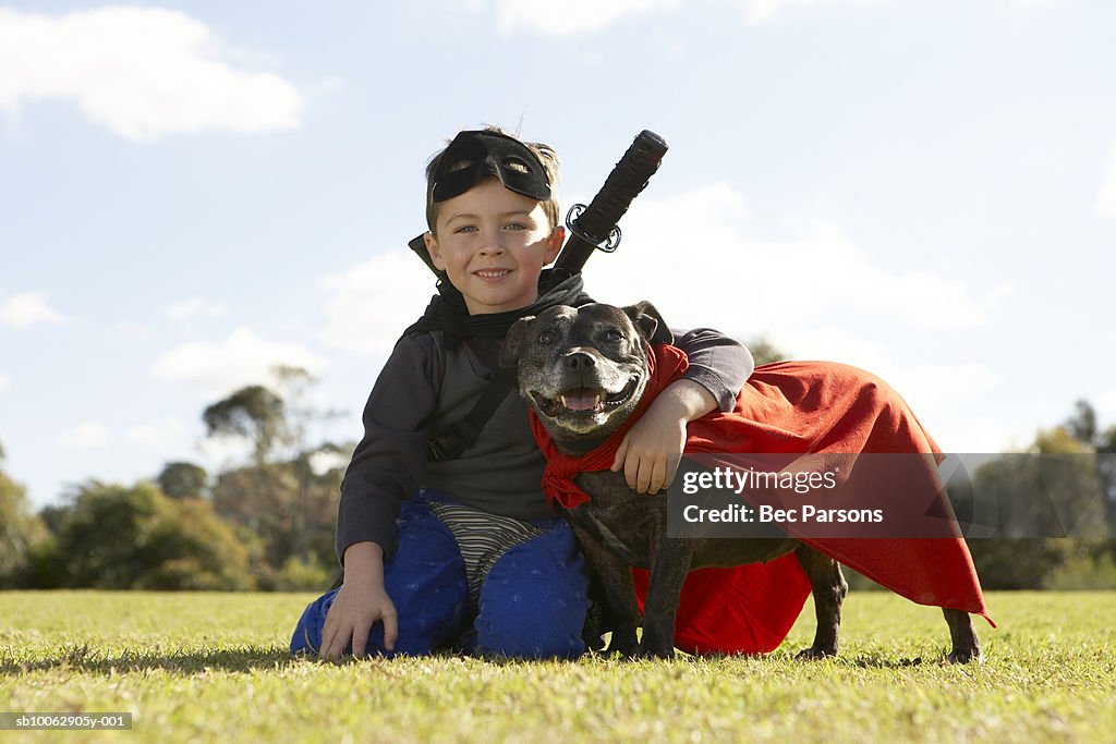 Boy (6-7) wearing costume, sitting with dog in park (surface level), portrait