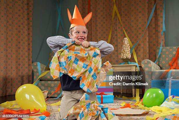 young boy (6-7) wearing party hat, making mess in room after party - spoilt children stock-fotos und bilder