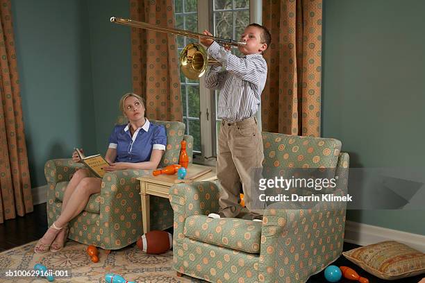 boy (6-7) playing trombone in living room, mother sitting beside and watching - trombone stock pictures, royalty-free photos & images