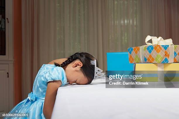 young girl (6-7 years) wearing dress and tiara, sleeping with head on table by birthday present - head on table stock-fotos und bilder