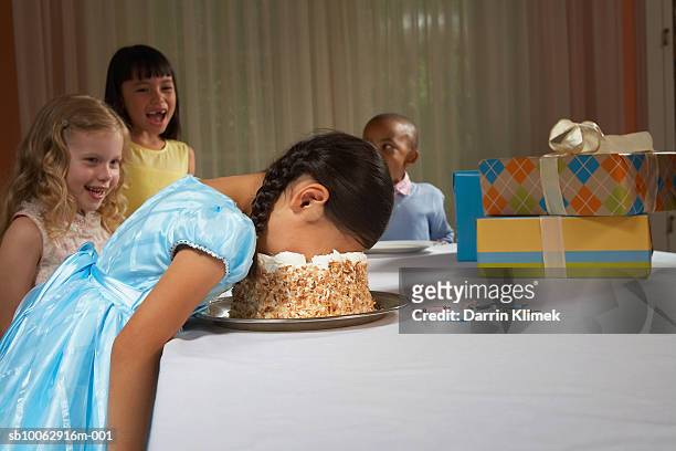 four children (5-8) at table, laughing at girl with face in cake - kids birthday party foto e immagini stock