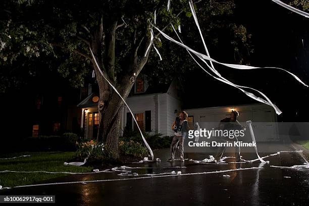 two boys (12-13) throwing toilet paper into tree in front of house, night - childish stock-fotos und bilder