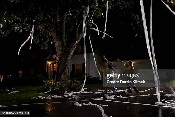 two girls (10-11, 12-13) throwing toilet paper into tree in front of house, night - naughty halloween stock pictures, royalty-free photos & images