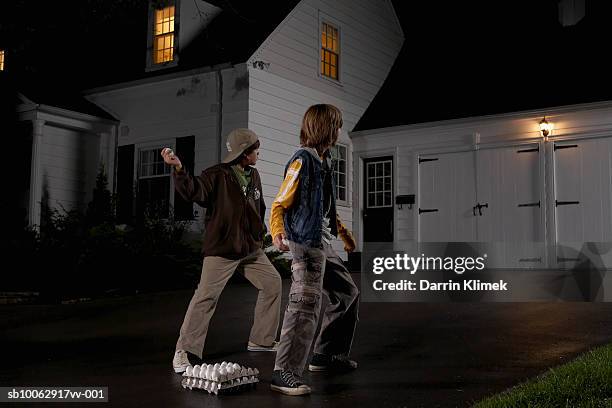 two boys (12-13) standing in driveway, throwing eggs at house, night, rear view - naughty halloween stock pictures, royalty-free photos & images