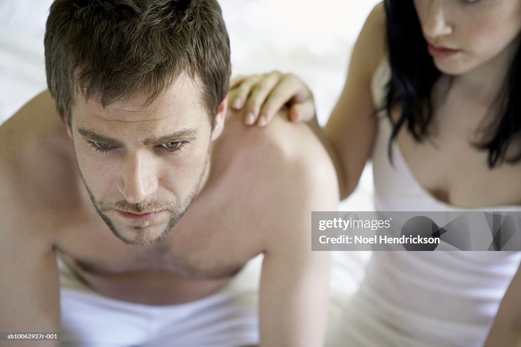 Young couple sitting at edge of bed, man worried, high angle view