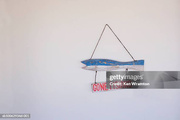 wooden sign in shape of fish saying 'gone fishing' hanging on white wall - gone fishing sign stockfoto's en -beelden