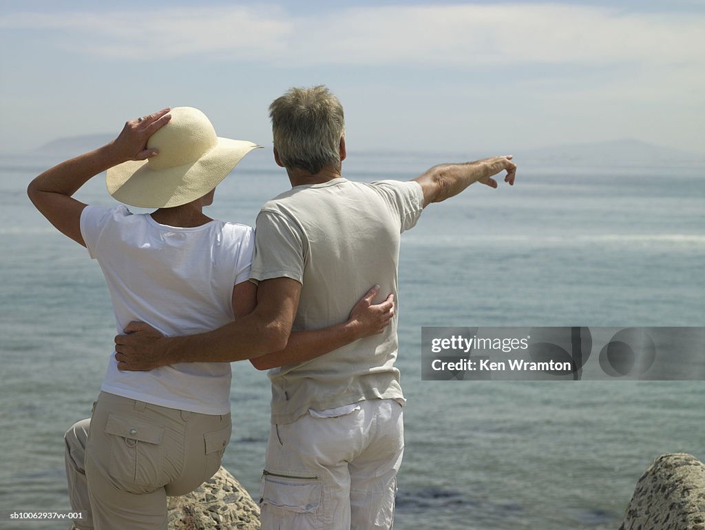 Mature couple embracing, facing sea, rear view