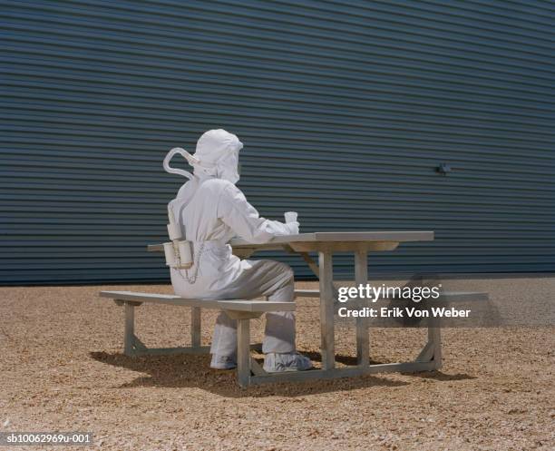 man in protective suit sitting at picnic table - stralingspak stockfoto's en -beelden