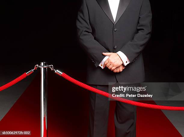 bouncer security man standing on red carpet by ropes, mid section - doorman stockfoto's en -beelden