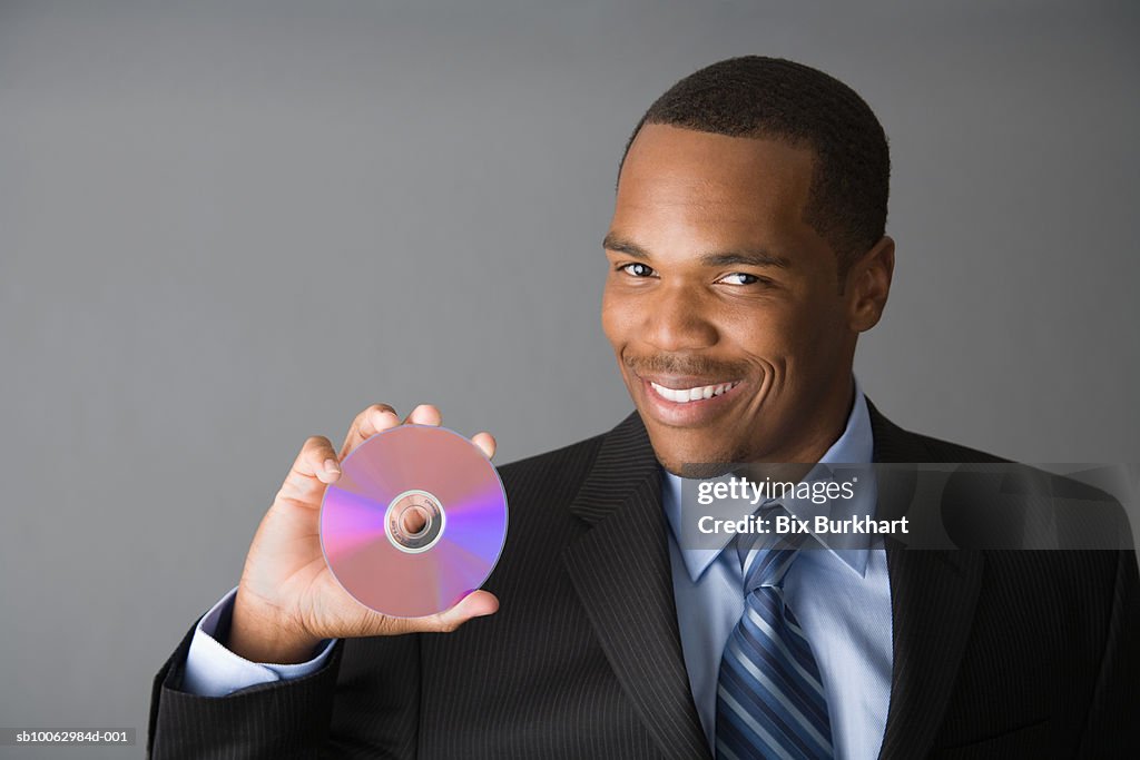 Portrait of young business man holding compact disc, smiling