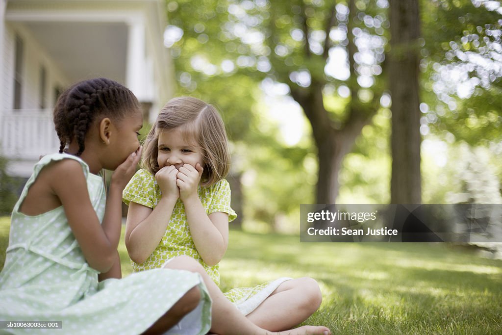 Two young girls (7-8 years) sitting at lawn in front of house, laughing