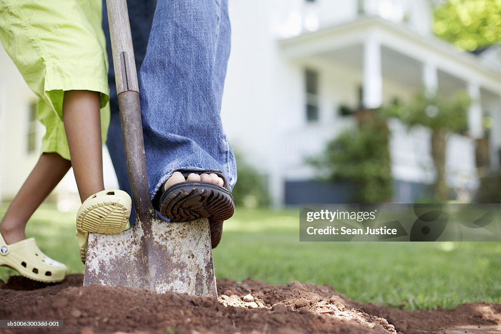 Man and young girl (8-9 years) digging soil in yard, low section