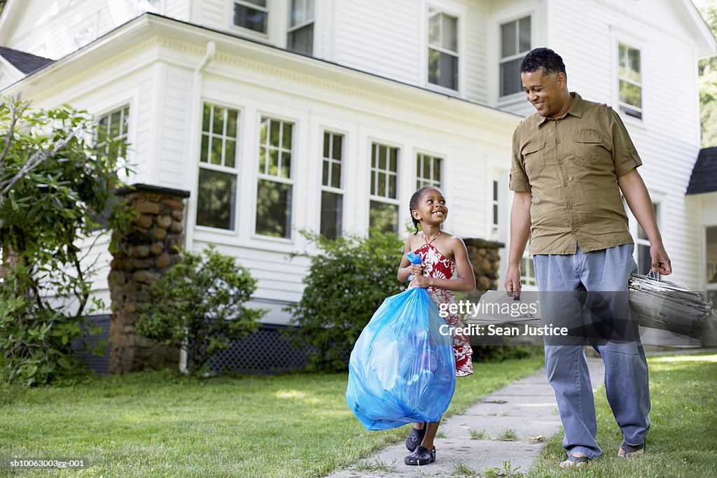 Father and daughter (8-9 years) carrying garbage bag in front of house